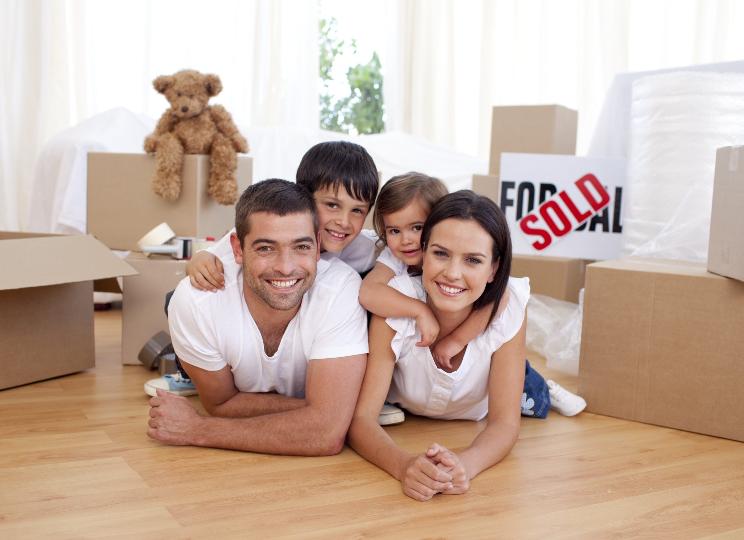 Family laying on new homes floor while packing (smiling at camera)