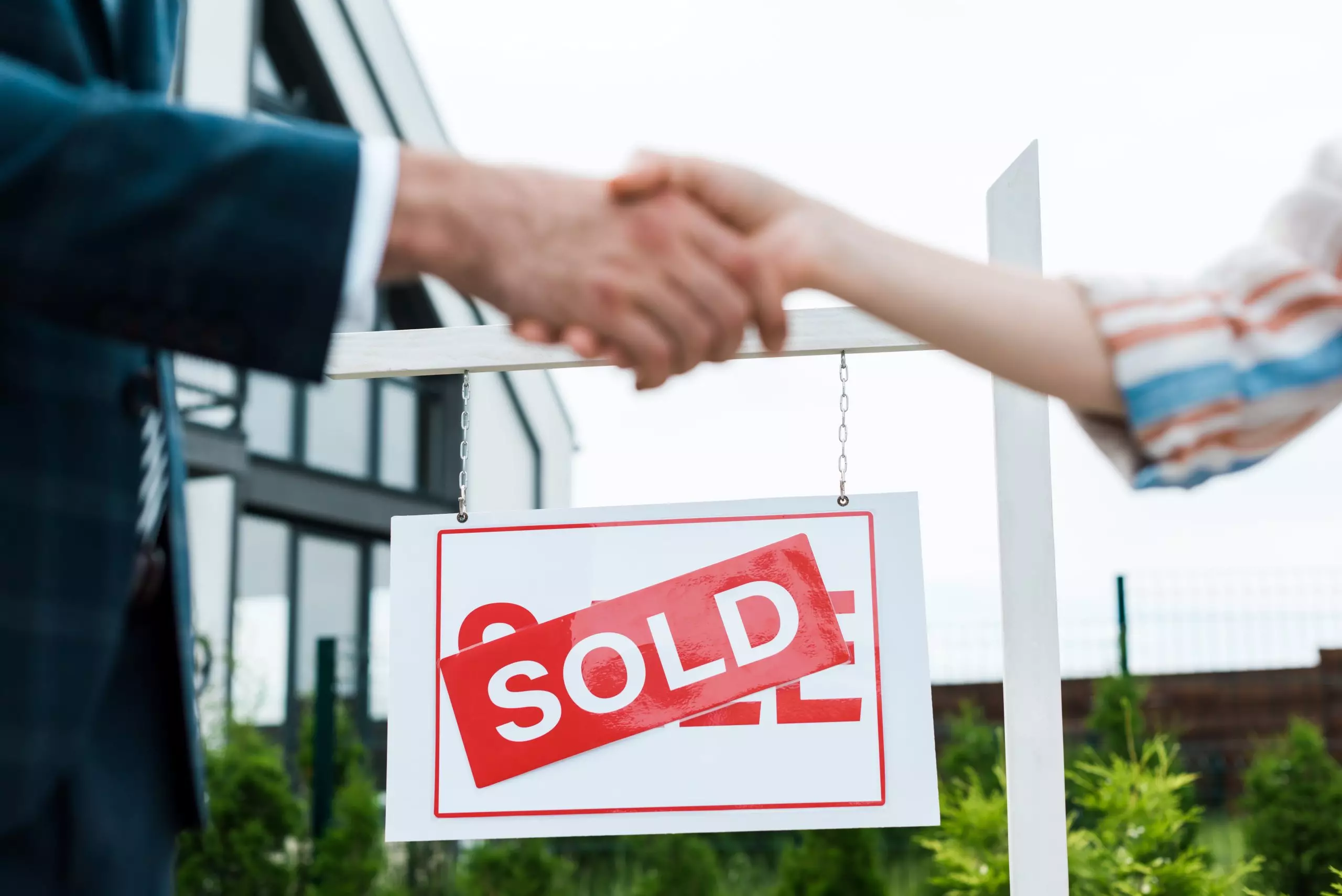 Blurred hands shaking in front of in focus house sold sign